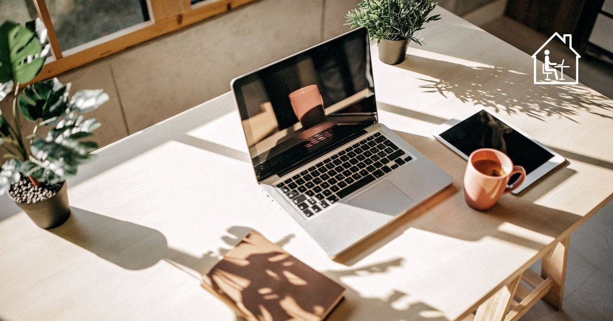 Ein Laptop, Tablet und Kaffee befinden sich auf einem Tisch. Diese symbolisieren mit dem Haus Icon Homeoffice. 