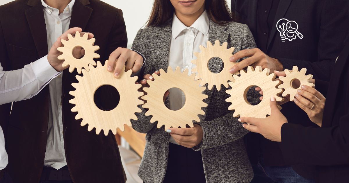 Mehrere Personen halten hölzerne Zahnräder, die symbolisch ineinandergreifen, und repräsentieren damit Zusammenarbeit und Teamentwicklung.